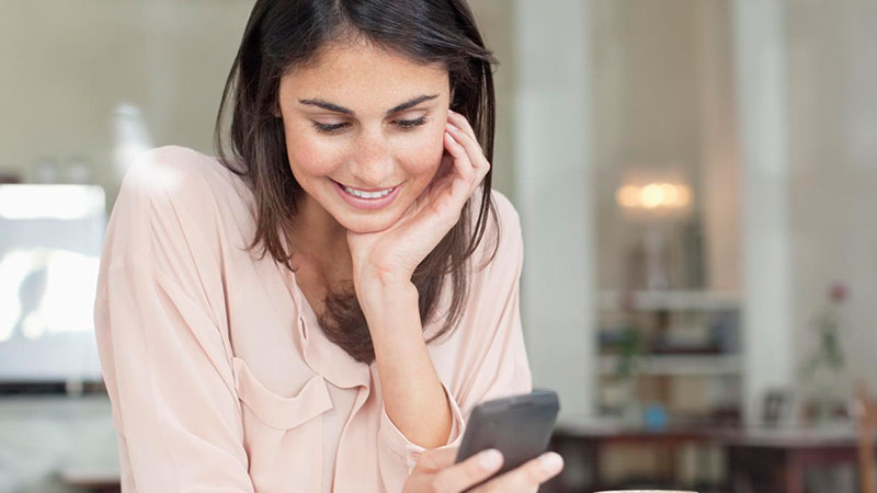 woman smiling with hand on face using mobile phone